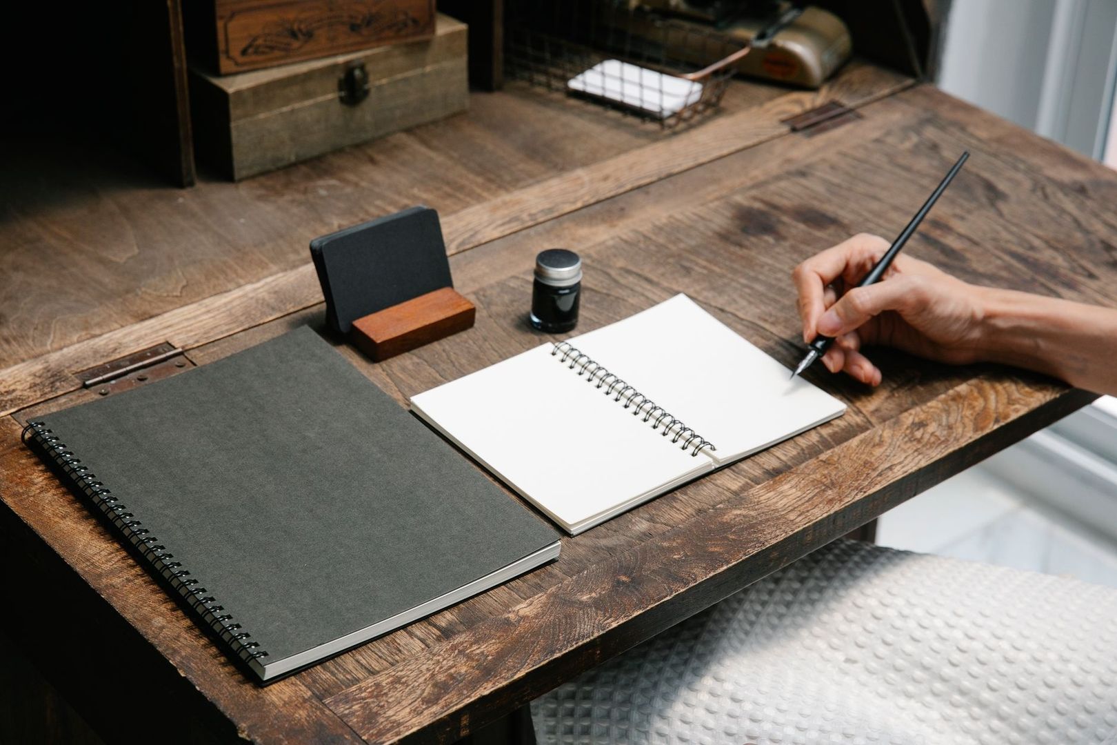 Hand schrijft met een pen in een leeg notitieboek op een houten bureau